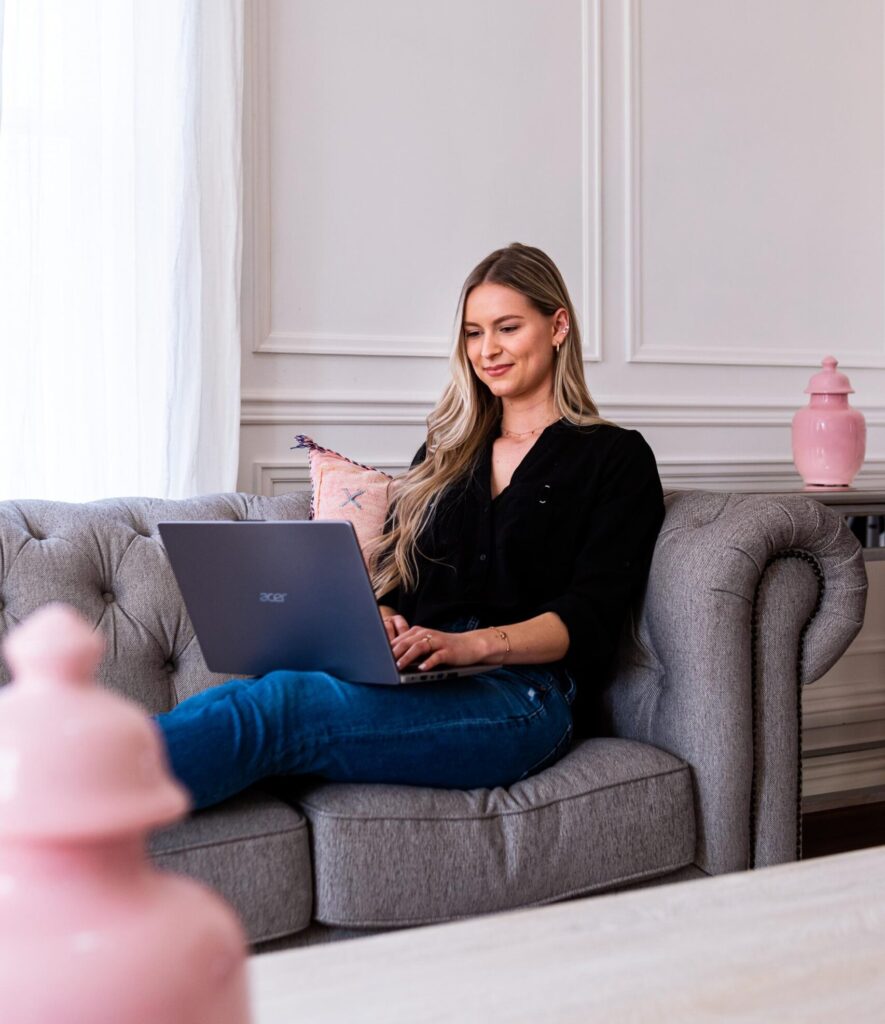 Kendra sitting on a couch working on her laptop